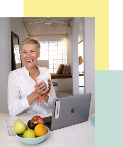 Porträt einer lachenden Frau mit Kaffeetasse am Laptop, auf dem Tisch ein Obstteller. Ausdruck von Lebensfreude und Professionalität.